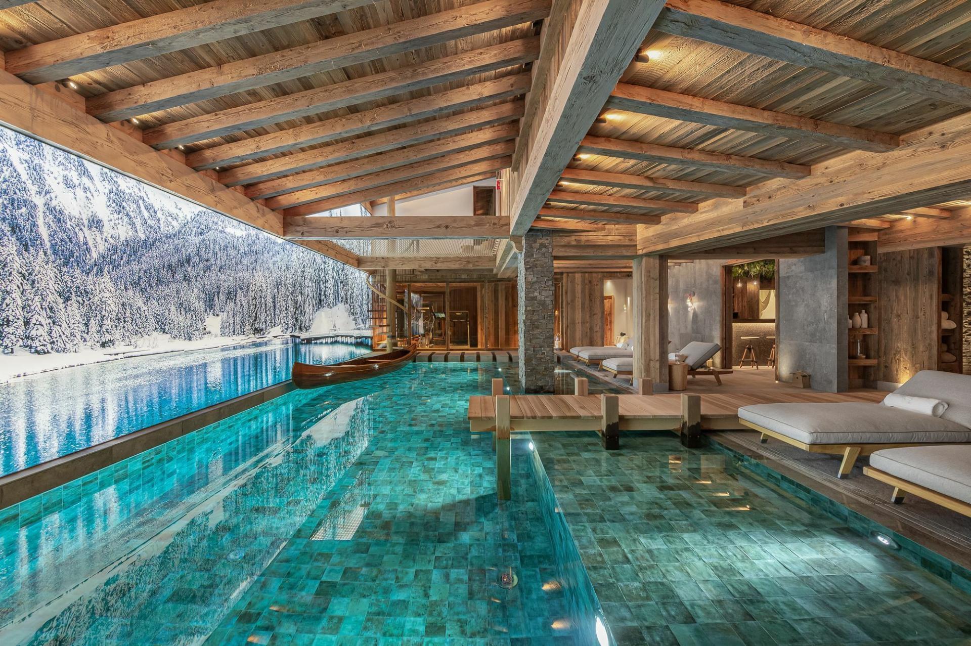 Luxury Swimming Pool in Chalet Bruxellois, designed to mimic a mountain lake. Pictured is the pool with a small jetty and boat, a truly unique ski chalet with a swimming pool.
