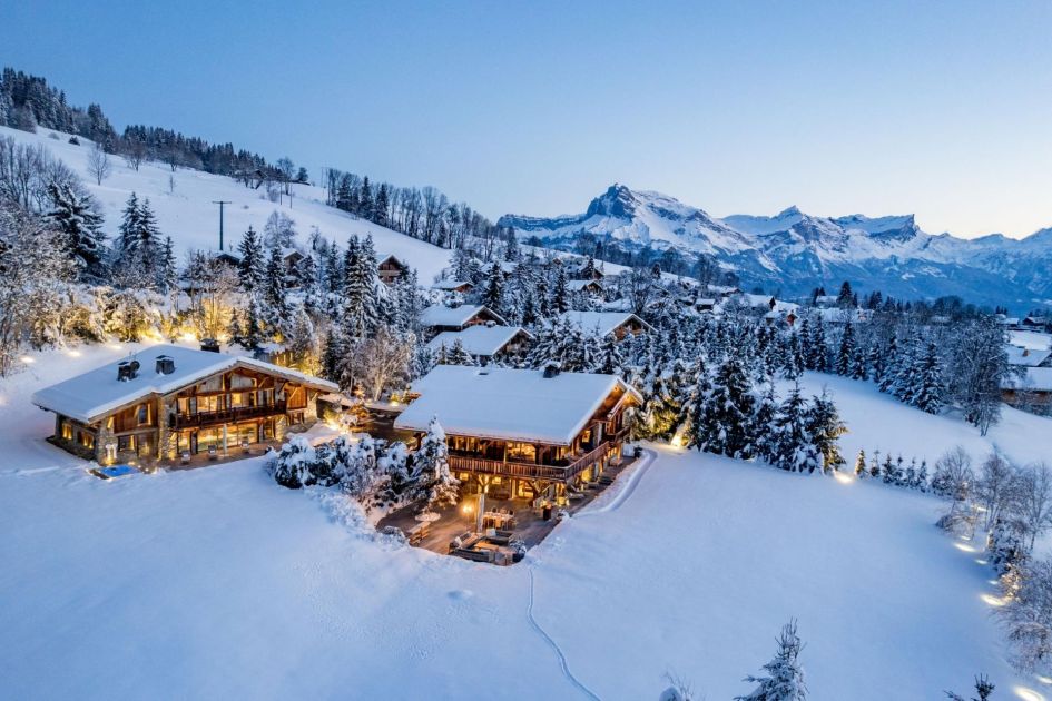 Ultima Megeve's two buildings lit up with mountain views in the distance.