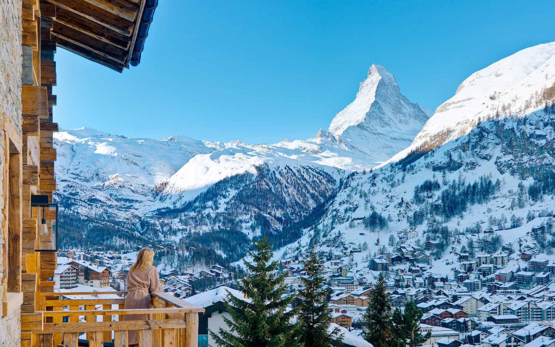 A woman looking out from a the balcony Chalet Les Anges, a luxury catered chalet in Zermatt, with a view of the Matterhorn