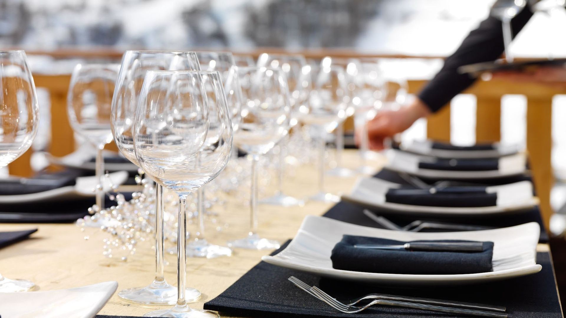 Alfresco table setting, with wine glasses and a hand of a highly trained staff member