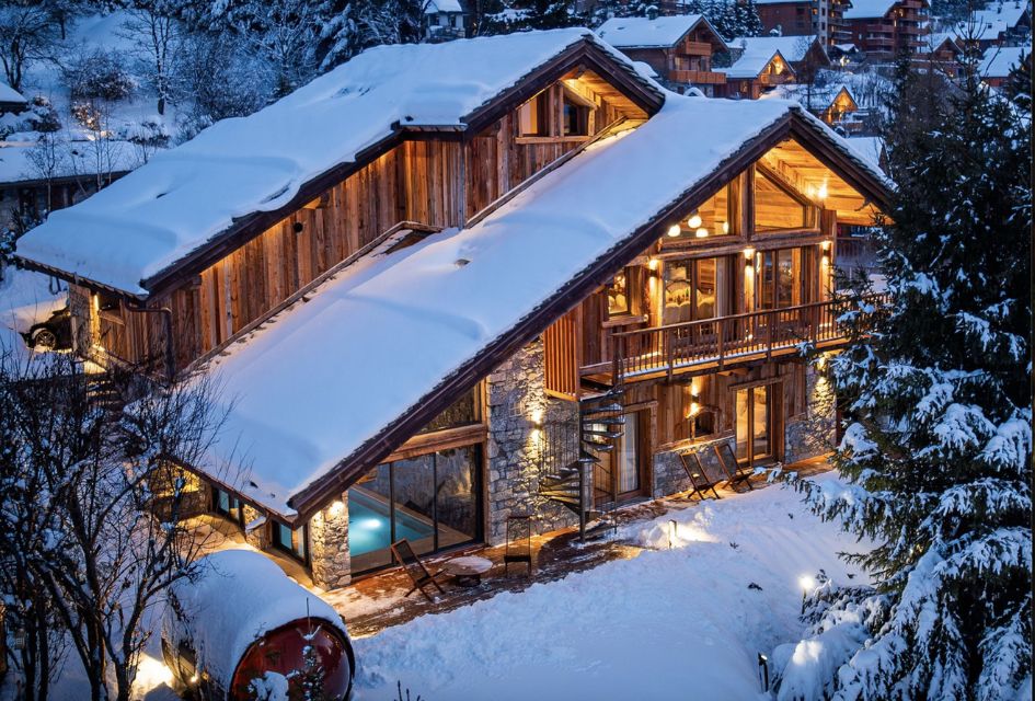 Chalet Ménor, Méribel Exterior of Chalet Ménor at dusk, surrounded by snow and with atmospheric lighting glowing through the chalet. The indoor pool and outdoor sauna is also visible.