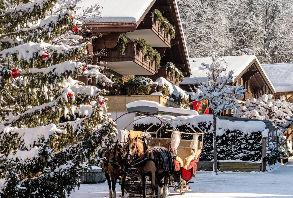 Gstaad at Christmas, with baubles on a snowy evergreen tree and horses ready to pull a carriage