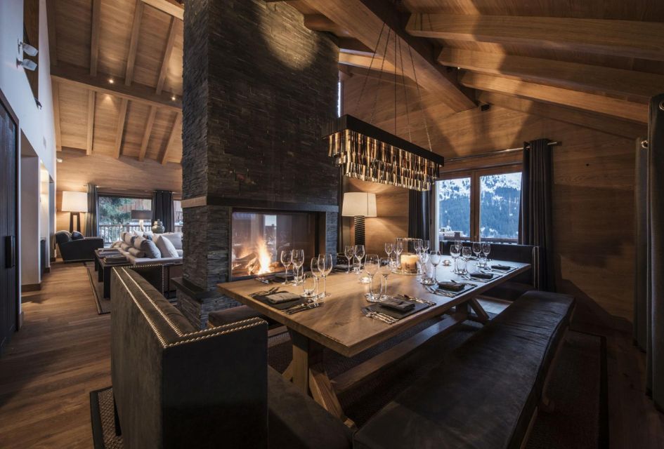 Chalet Grenier, Méribel Interior dining area of Chalet Le Grenier, with the central fireplace blazing and the modern chandelier above the table laid for dinner