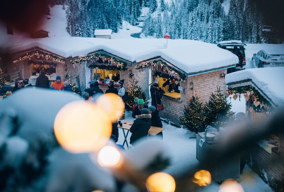 Stalls at the Christmas markets in Lech, one of the top ski resorts for Christmas, with ski lifts in the background and snow covering stall roofs