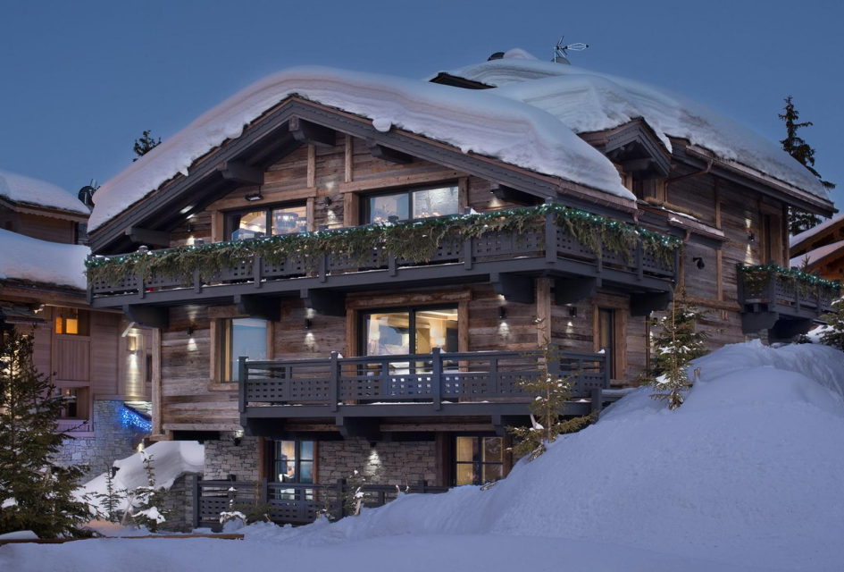 Exterior at dusk of Le Petit Palais, an impressive luxury ski-in, ski-out chalet in Courchevel 1850. Its sparkling lights invite in from the snow outside, and on the roof.