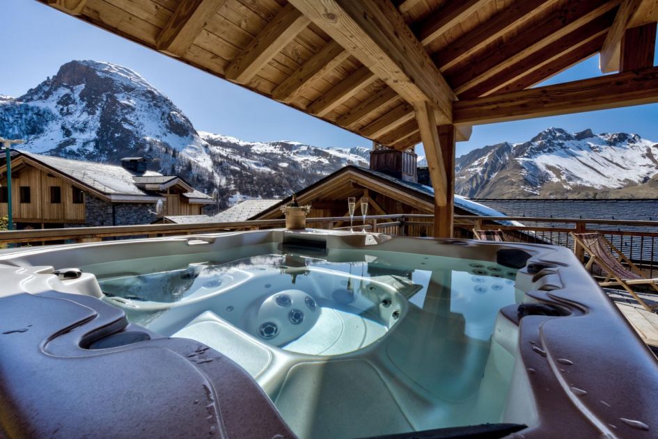 Chez Bugi's outdoor hot tub sits on the covered terrace with views of the surrounding mountains in the distance - the perfect wellness facility that awaits your return back to this ski-in, ski-out chalet!