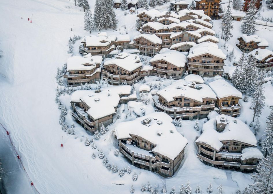 The collection of Le K2 Chalets with snow-topped wooden exteriors standing amongst the snowy scenery and fir trees. Beside lies the blue Cospillot piste which makes this group some of the best ski-in, ski-out chalets in France.