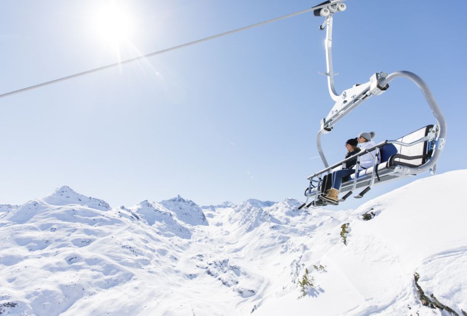 Pedestrians riding a chairlift over the snowy mountains under the sun in Meribel.