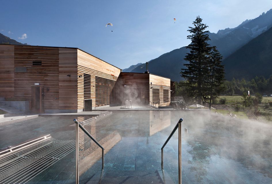 Steaming outdoor pool of QC Terme Spa Chamonix Mont Blanc with paragliders in the blue skies above